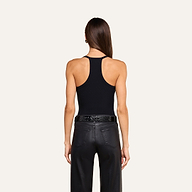 A woman with straight brown hair wearing the Wrenna Racerback Bodysuit, black pants, and a black belt stands facing away on a light background.