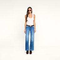 A woman wearing sunglasses, blue jeans with a black belt, and dark shoes stands against a plain white background, styled in the Shania Racerback Tank.