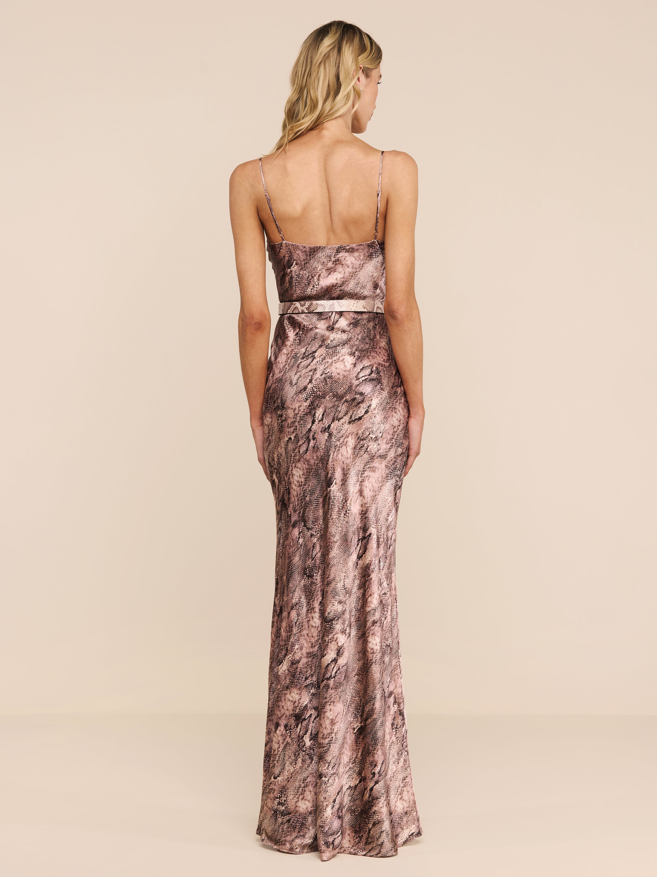 A woman stands facing away against a plain white background, wearing the Serita Silk Gown—a long, form-fitting slip dress featuring a pink and brown marble pattern.