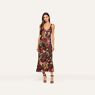 A woman wearing the Akiya Satin Maxi Dress—a sleeveless, ankle-length tank dress featuring a colorful statement collage print—stands against a plain light background with black strappy heels.