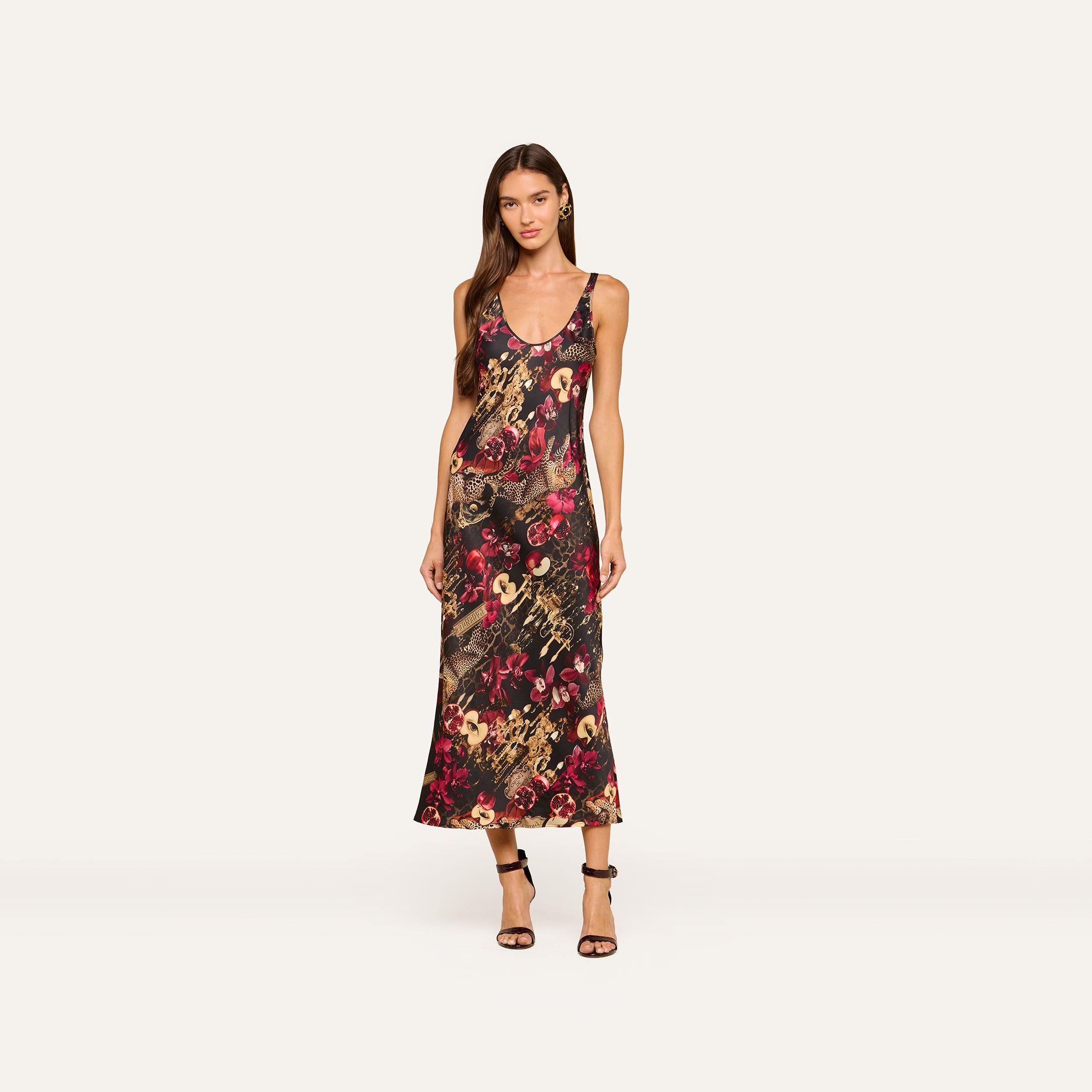 A woman wearing the Akiya Satin Maxi Dress—a sleeveless, ankle-length tank dress featuring a colorful statement collage print—stands against a plain light background with black strappy heels.