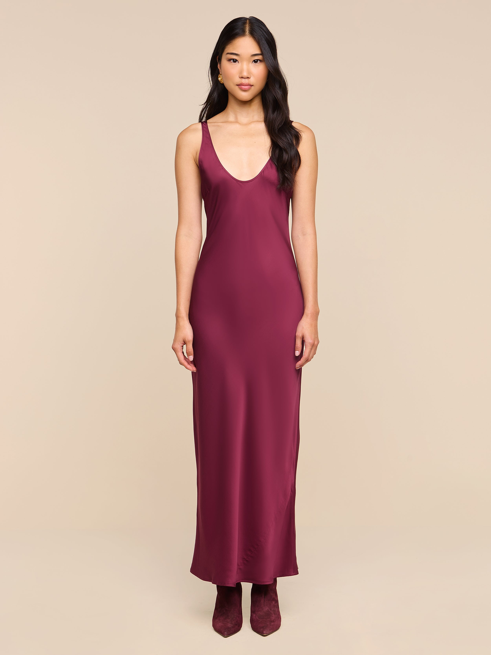 A woman stands facing forward, wearing the sleeveless, floor-length Akiya Satin Maxi Dress in deep burgundy with matching shoes, set against a plain white background.