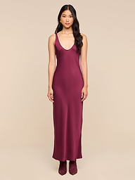 A woman stands facing forward, wearing the sleeveless, floor-length Akiya Satin Maxi Dress in deep burgundy with matching shoes, set against a plain white background.