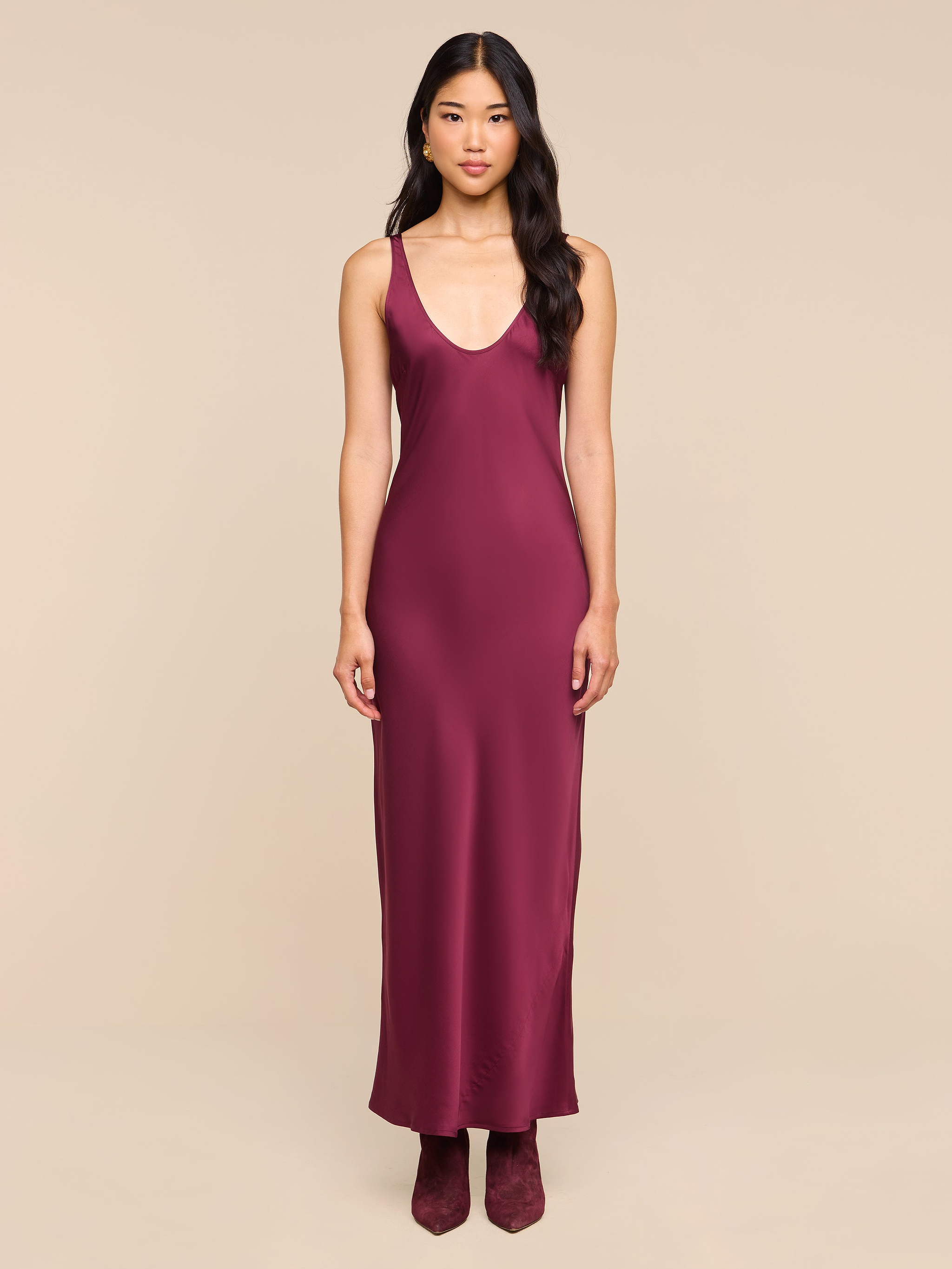 A woman stands facing forward, wearing the sleeveless, floor-length Akiya Satin Maxi Dress in deep burgundy with matching shoes, set against a plain white background.