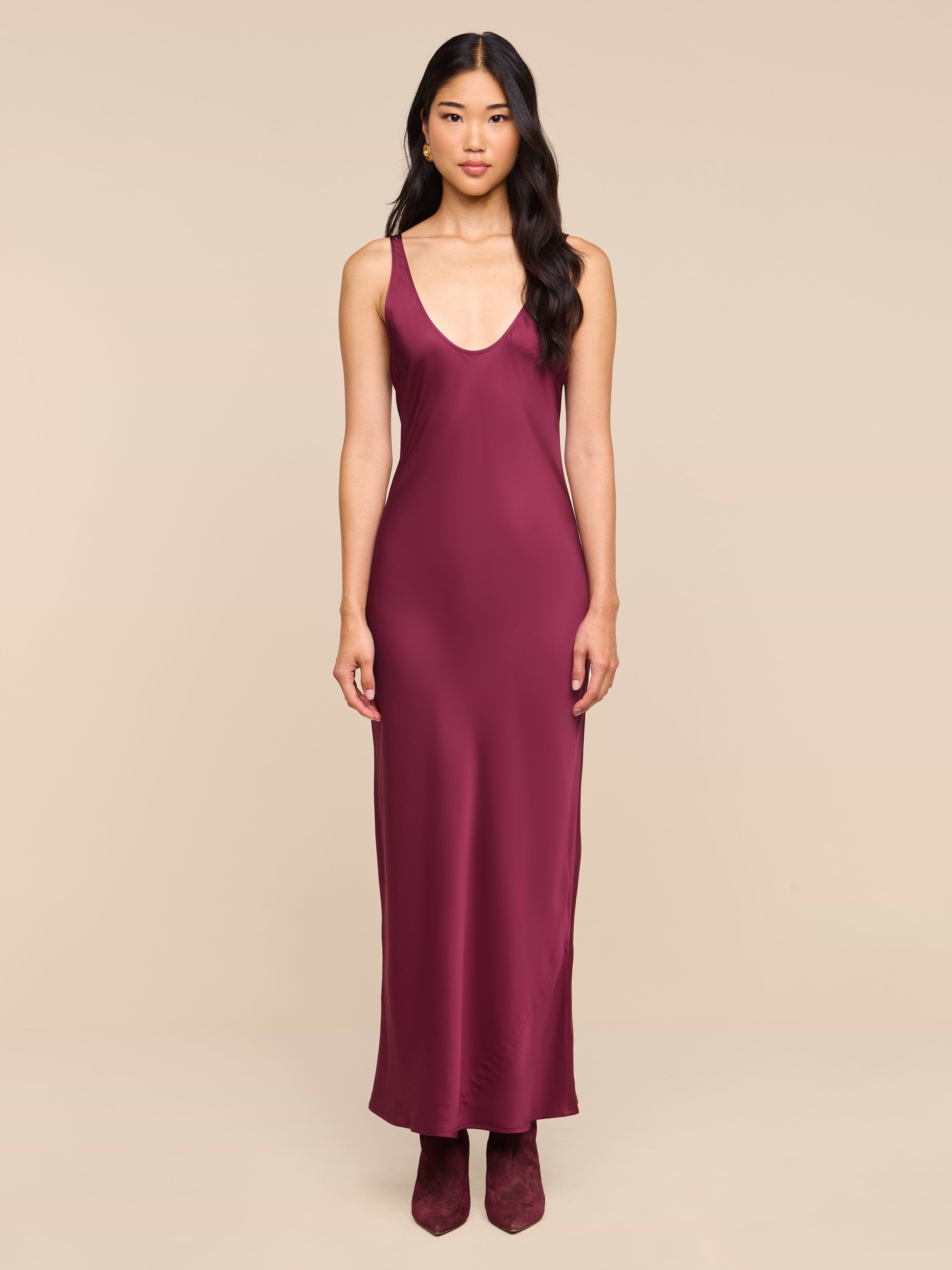 A woman stands facing forward, wearing the sleeveless, floor-length Akiya Satin Maxi Dress in deep burgundy with matching shoes, set against a plain white background.
