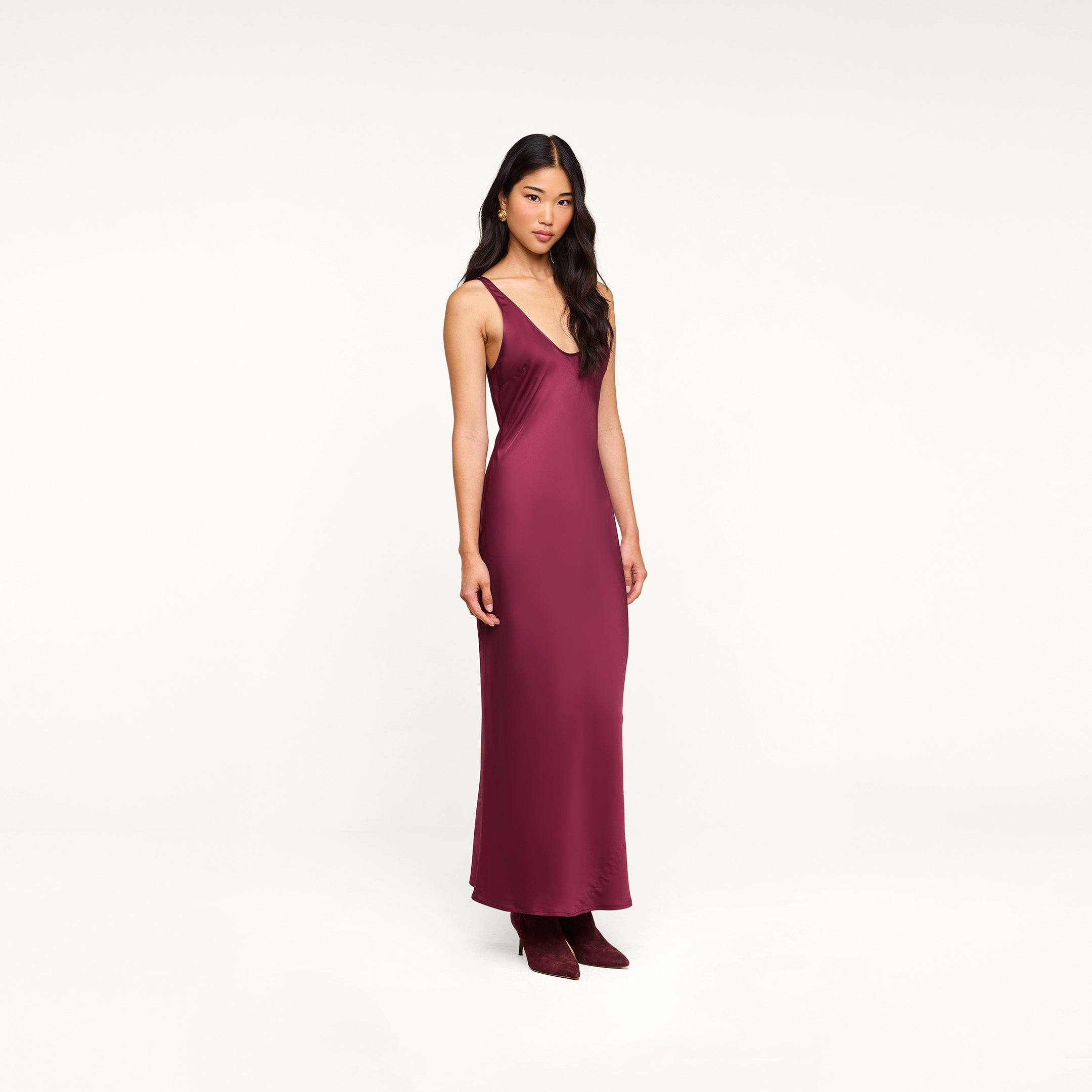 Wearing the Akiya Satin Maxi Dress in burgundy and matching shoes, a woman stands against a plain white background.