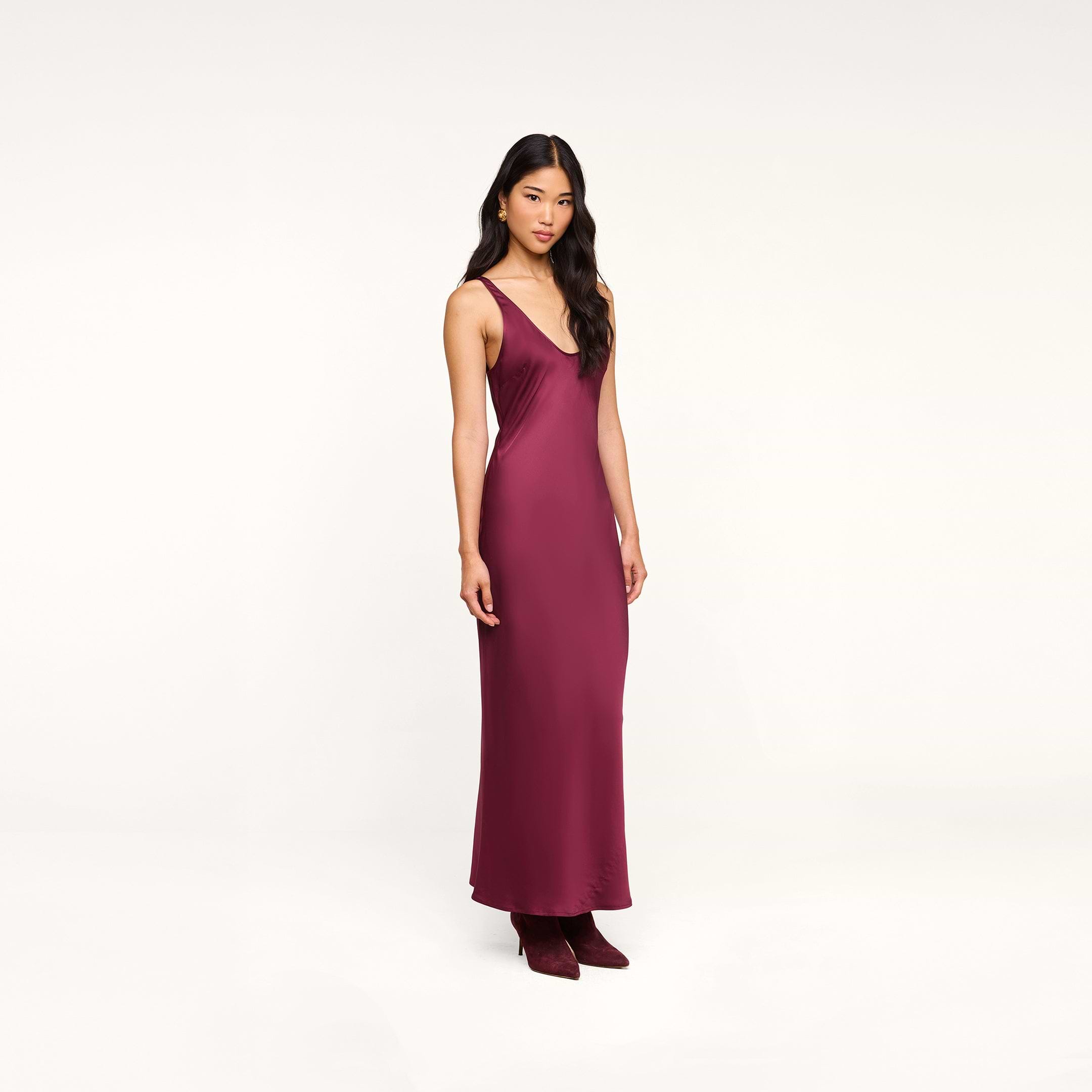 Wearing the Akiya Satin Maxi Dress in burgundy and matching shoes, a woman stands against a plain white background.