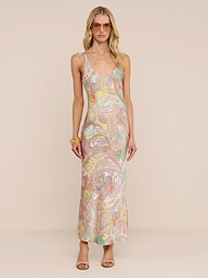 A woman in sunglasses and a long, sleeveless Akiya Satin Maxi Dress stands against a beige background. Her wavy blonde hair, chunky bracelet, and open-toe heels create a chic day-to-night look.