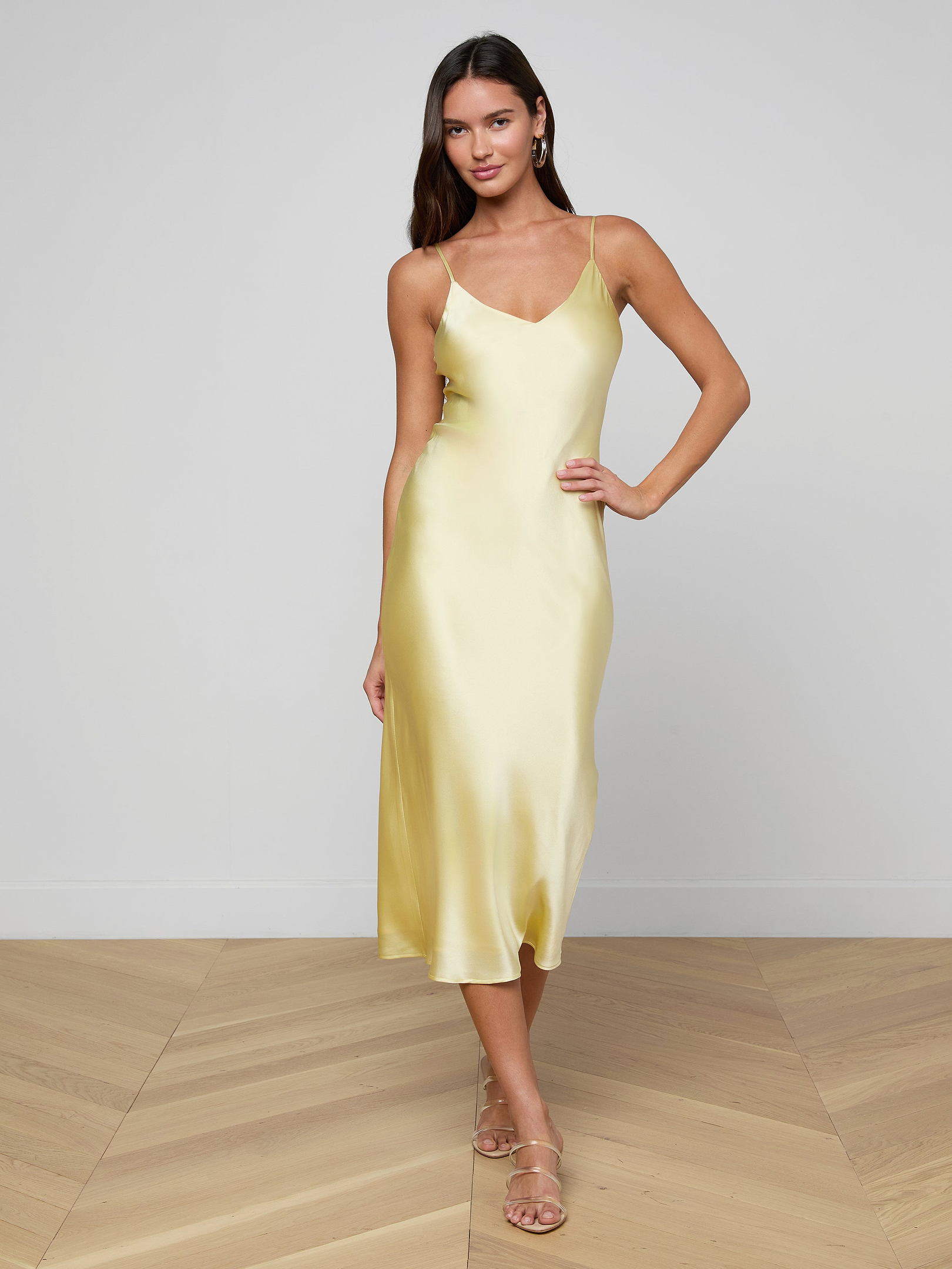 Wearing the Seridie Silk Slip Dress in yellow and beige sandals, a woman stands posing against a plain white background.