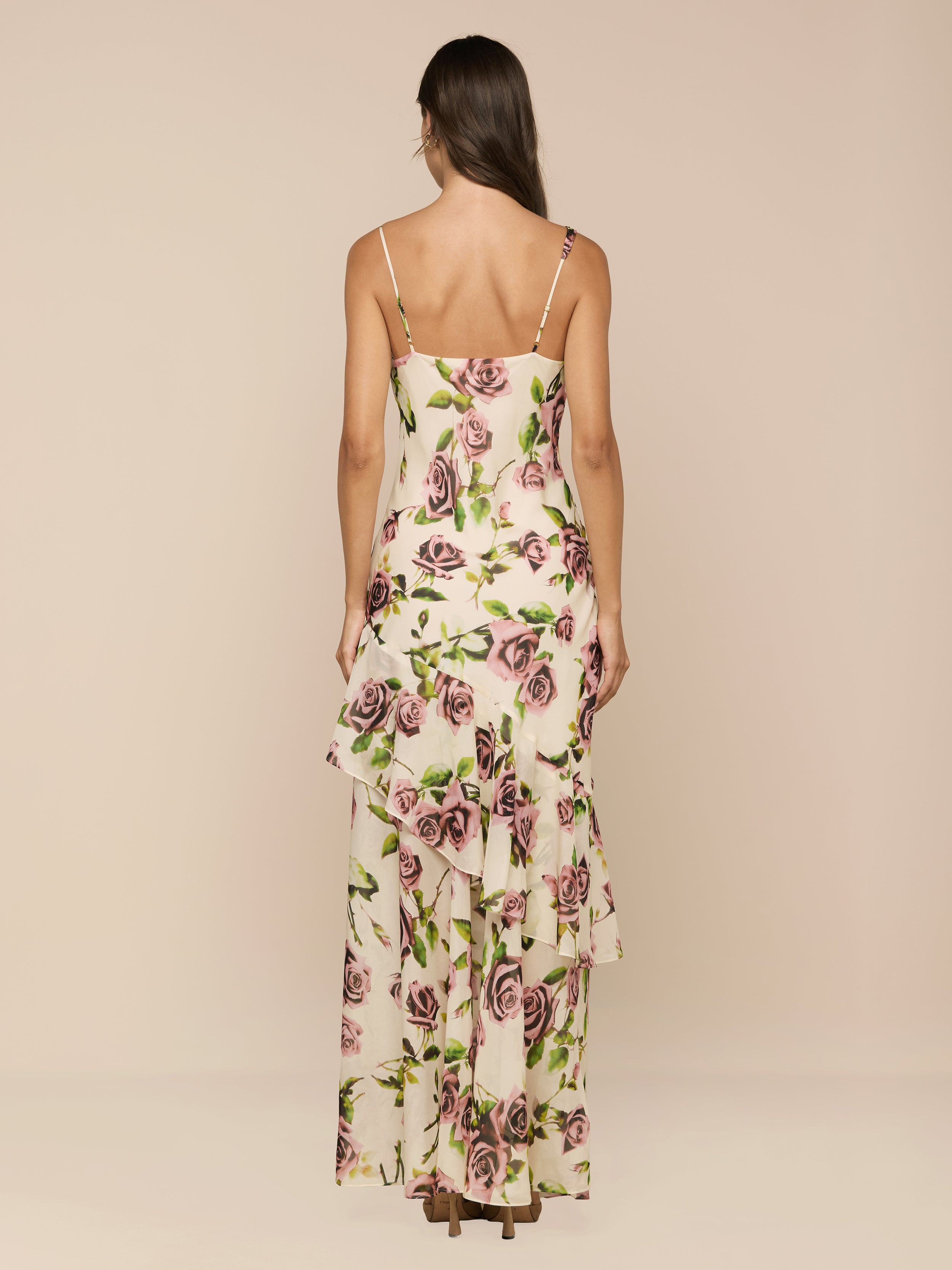 A woman is shown from behind wearing the Viola Silk Cowl-Neck Gown, a long, sleeveless silk chiffon dress with thin straps and layered ruffles in a mauve rose print, set against a plain white background.