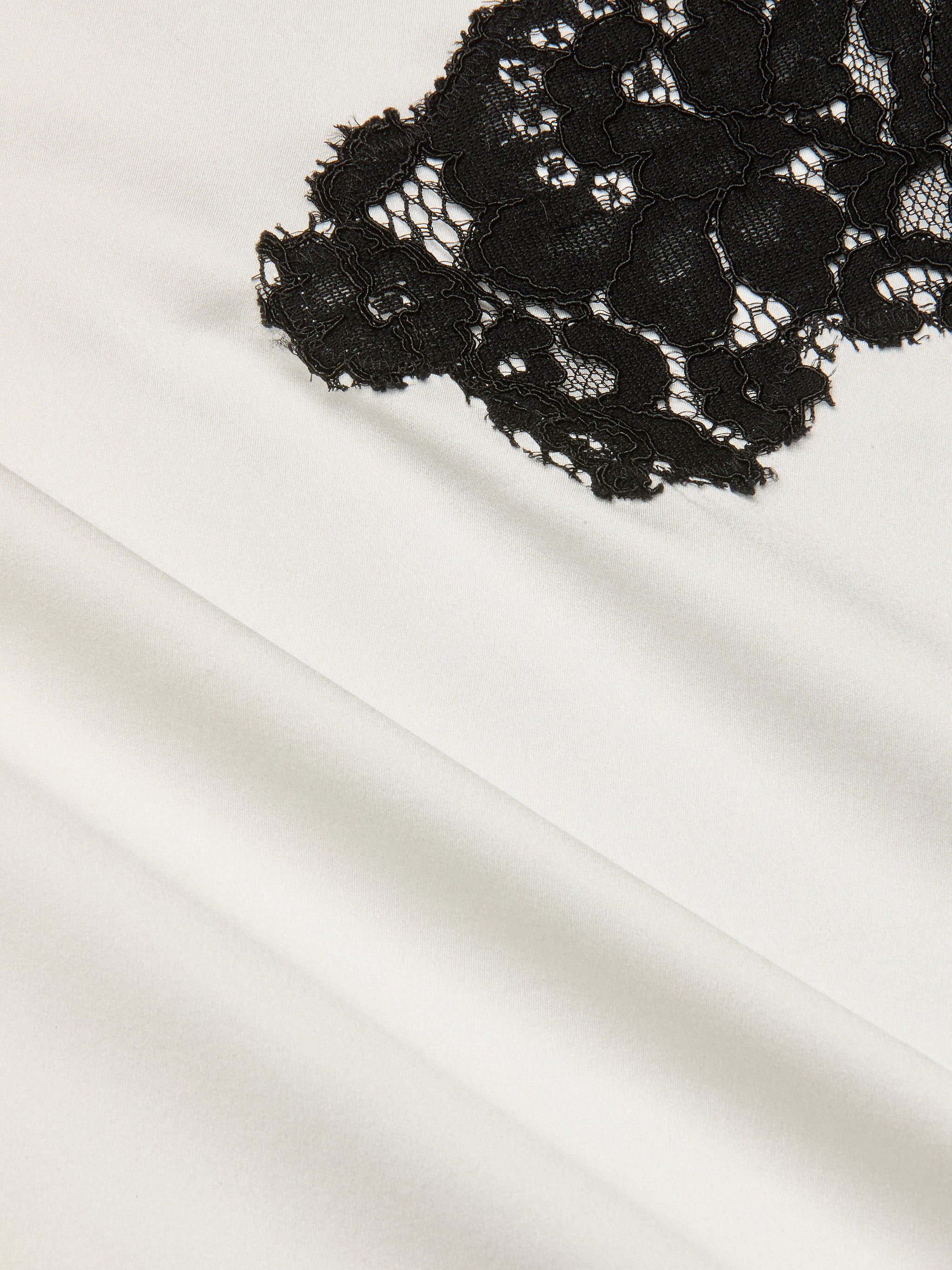 Close-up of black floral lace fabric layered over smooth, white silk charmeuse, showcasing the striking contrast in textures and colors that evoke the elegance of the Fenna Silk Lace Dress.