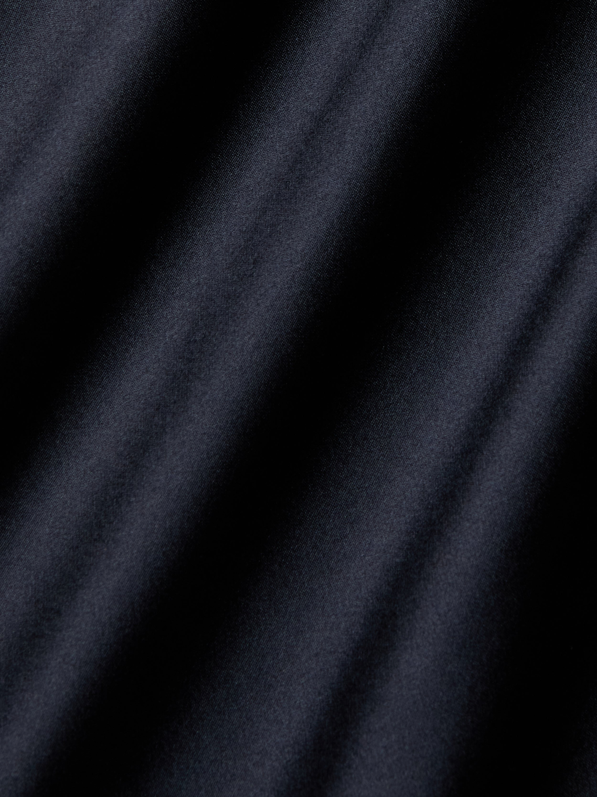 Close-up of smooth, dark fabric with diagonal, soft shadows creating a textured, wavy appearance—evocative of the luxurious Shayla Silk Lace Gown.
