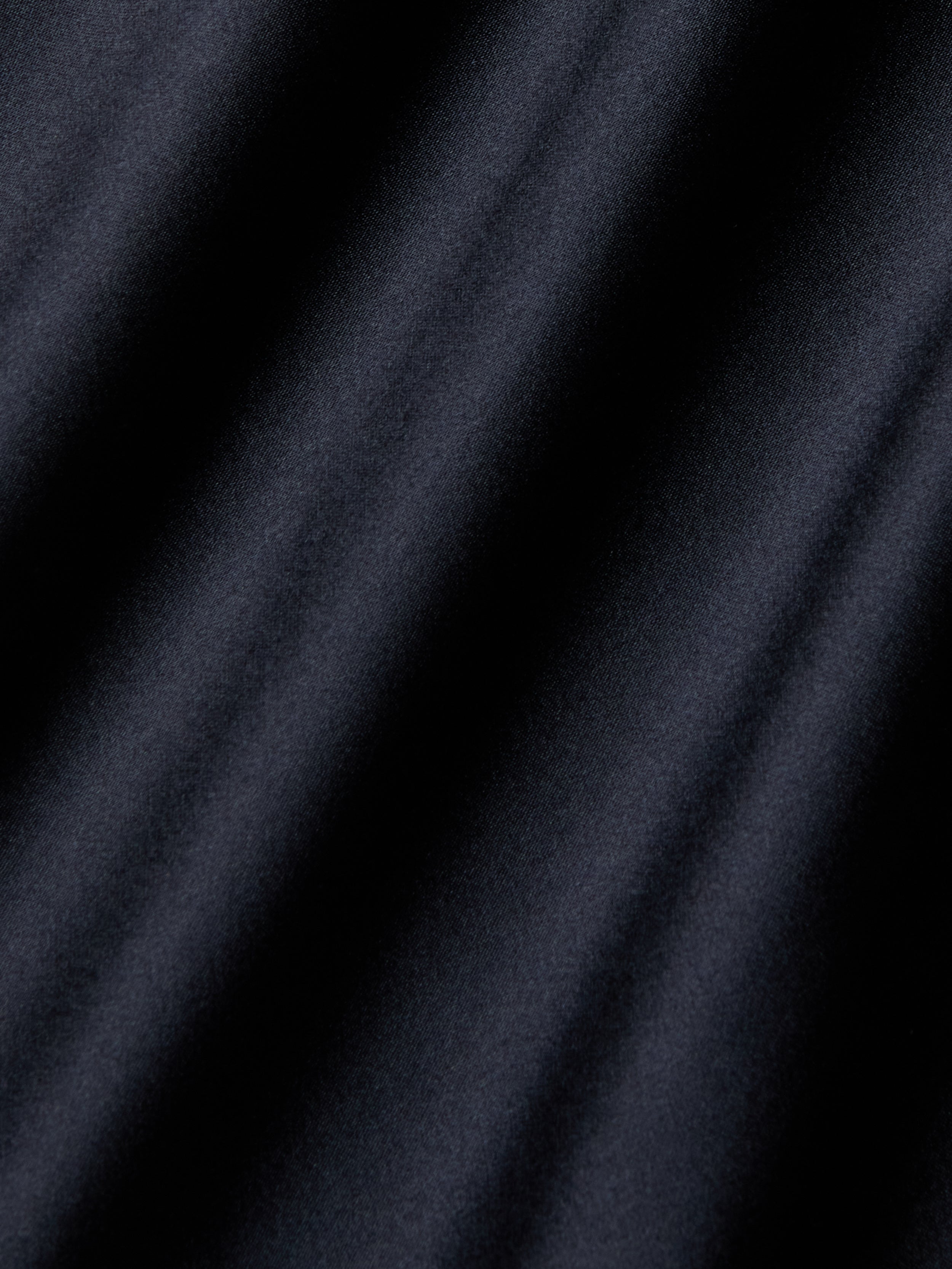 Close-up of smooth, dark fabric with diagonal, soft shadows creating a textured, wavy appearance—evocative of the luxurious Shayla Silk Lace Gown.