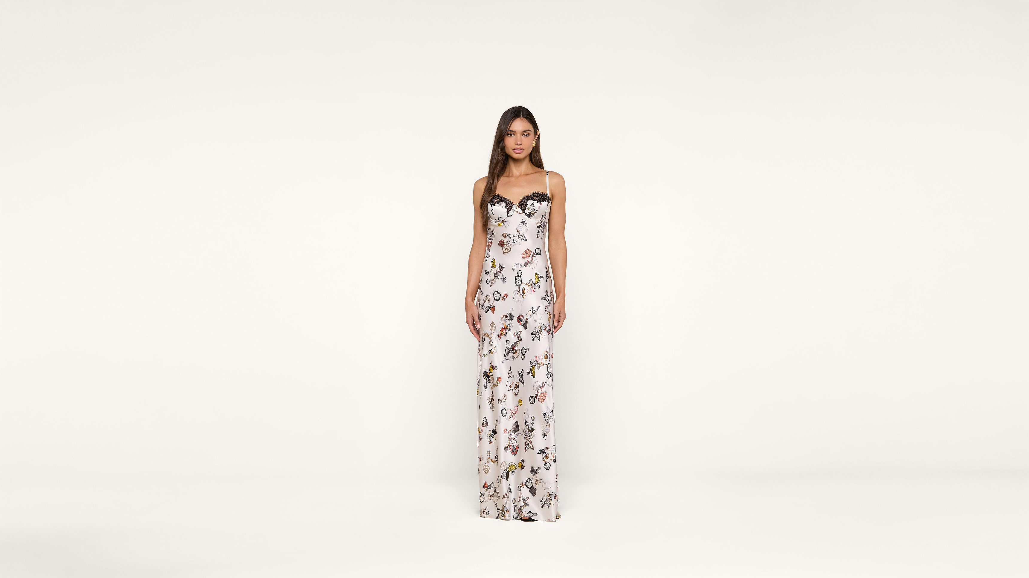 A woman stands against a plain white background, wearing a long, white, strapless dress with a colorful floral pattern.