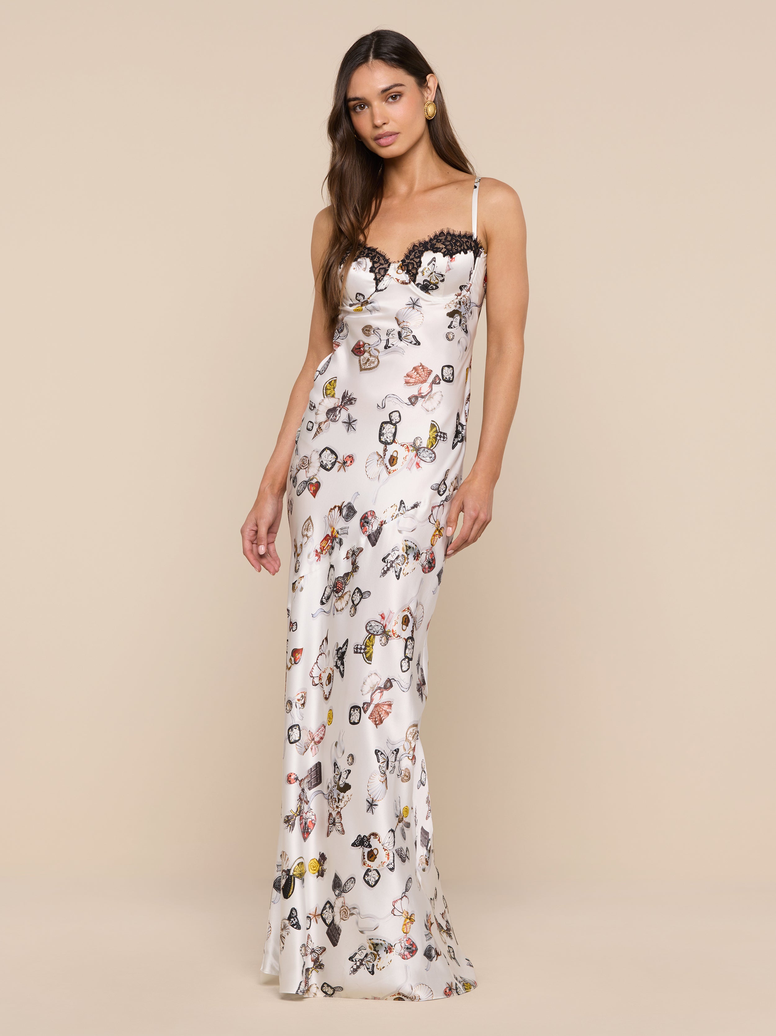 A woman wearing the Sayla Silk Gown—a long, white floral silk dress featuring black lace detailing at the bust—stands against a plain white background, evoking vintage glamour.