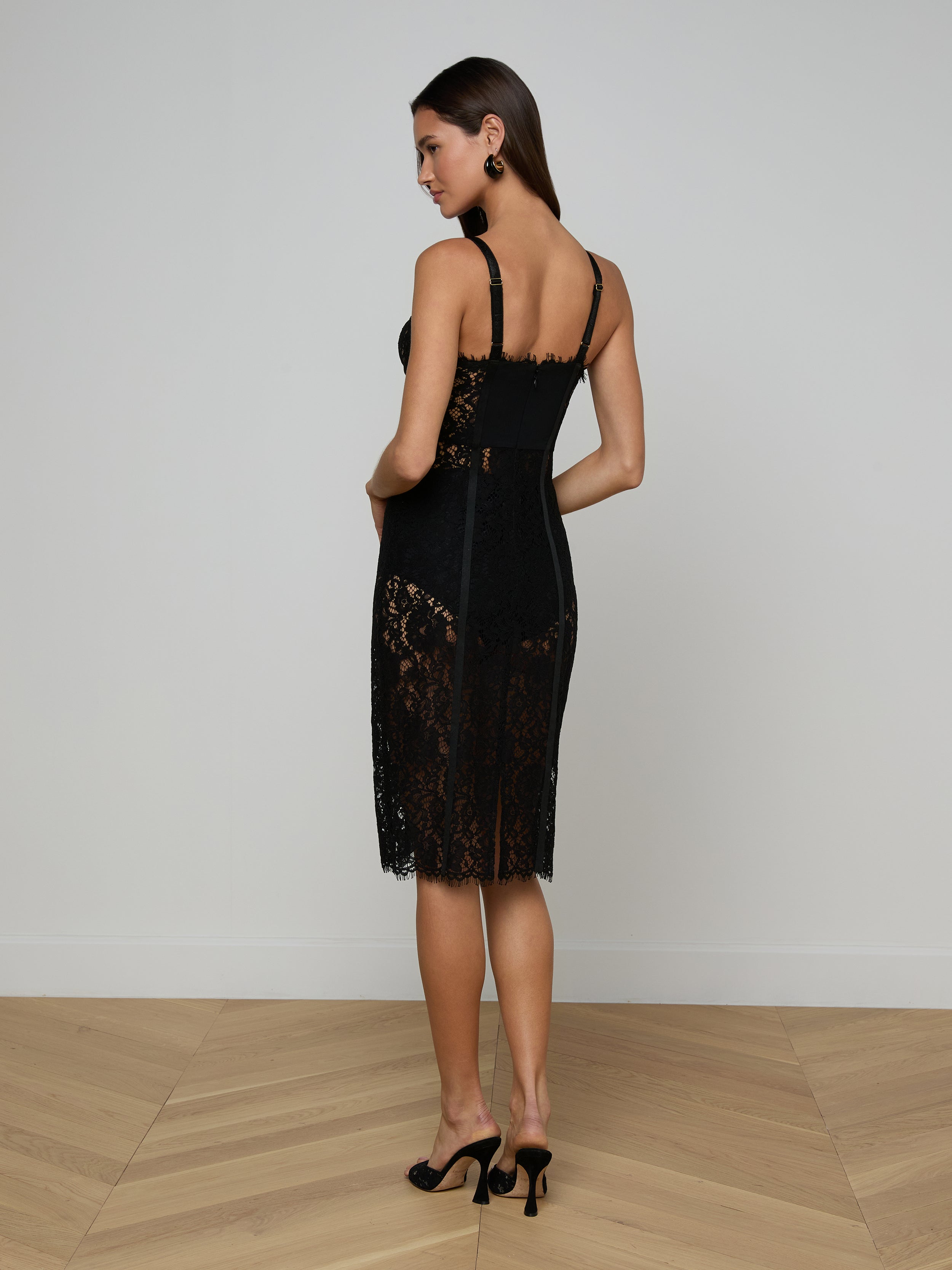 A woman in the Jennifer Lace Midi Dress, featuring sheer floral lace, and heels stands against a plain white background, facing away but looking over her shoulder.