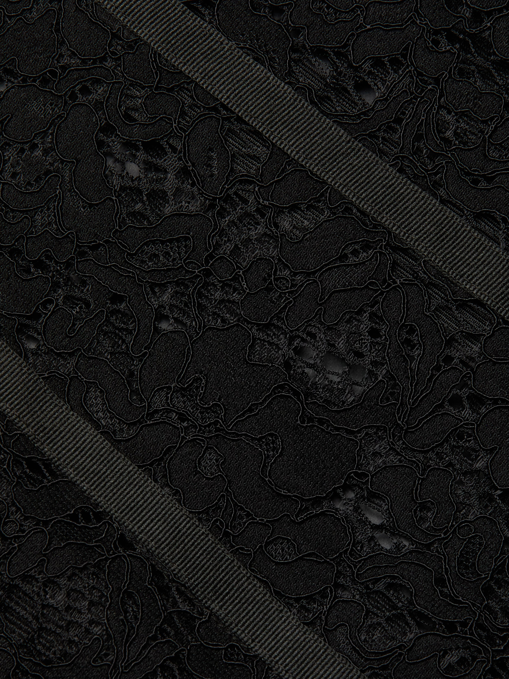 Close-up of the Jennifer Lace Midi Dress, featuring textured sheer floral lace fabric adorned with two diagonally crossing black grosgrain ribbons. The intricate floral pattern of the lace is beautifully contrasted by the ribbed surface of the ribbons, highlighting the delicate details of the dress.