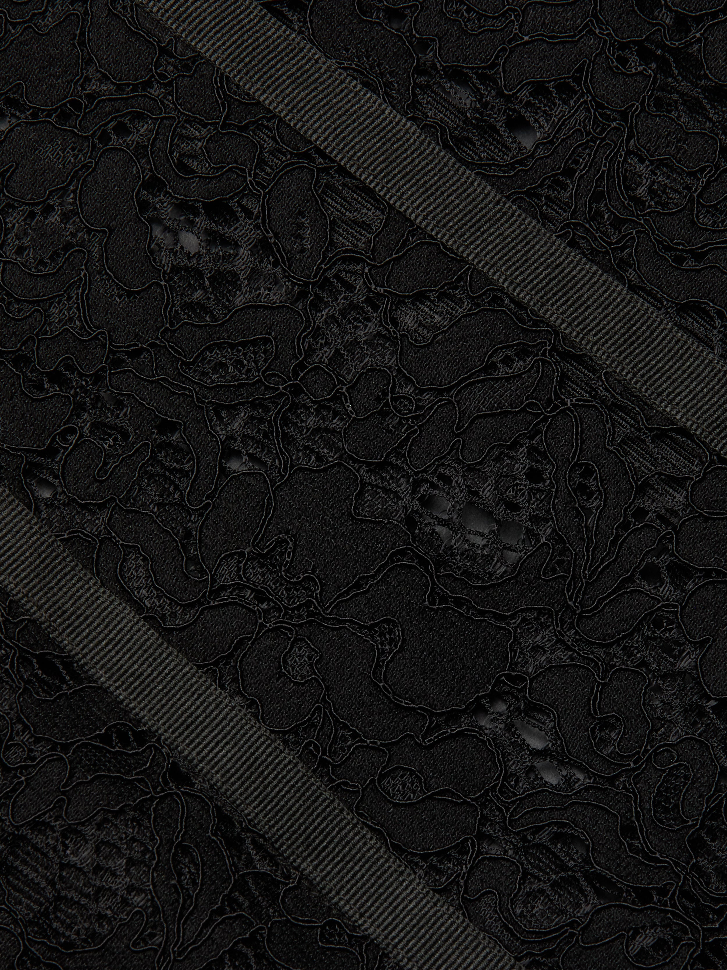 Close-up of the Jennifer Lace Midi Dress, featuring textured sheer floral lace fabric adorned with two diagonally crossing black grosgrain ribbons. The intricate floral pattern of the lace is beautifully contrasted by the ribbed surface of the ribbons, highlighting the delicate details of the dress.