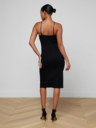 A woman with her hair in a bun wears the Eira Midi Dress—a fitted, sleeveless slip dress crafted from super stretch ponte—in black, paired with black heels. She stands with her back to the camera against a plain white background.