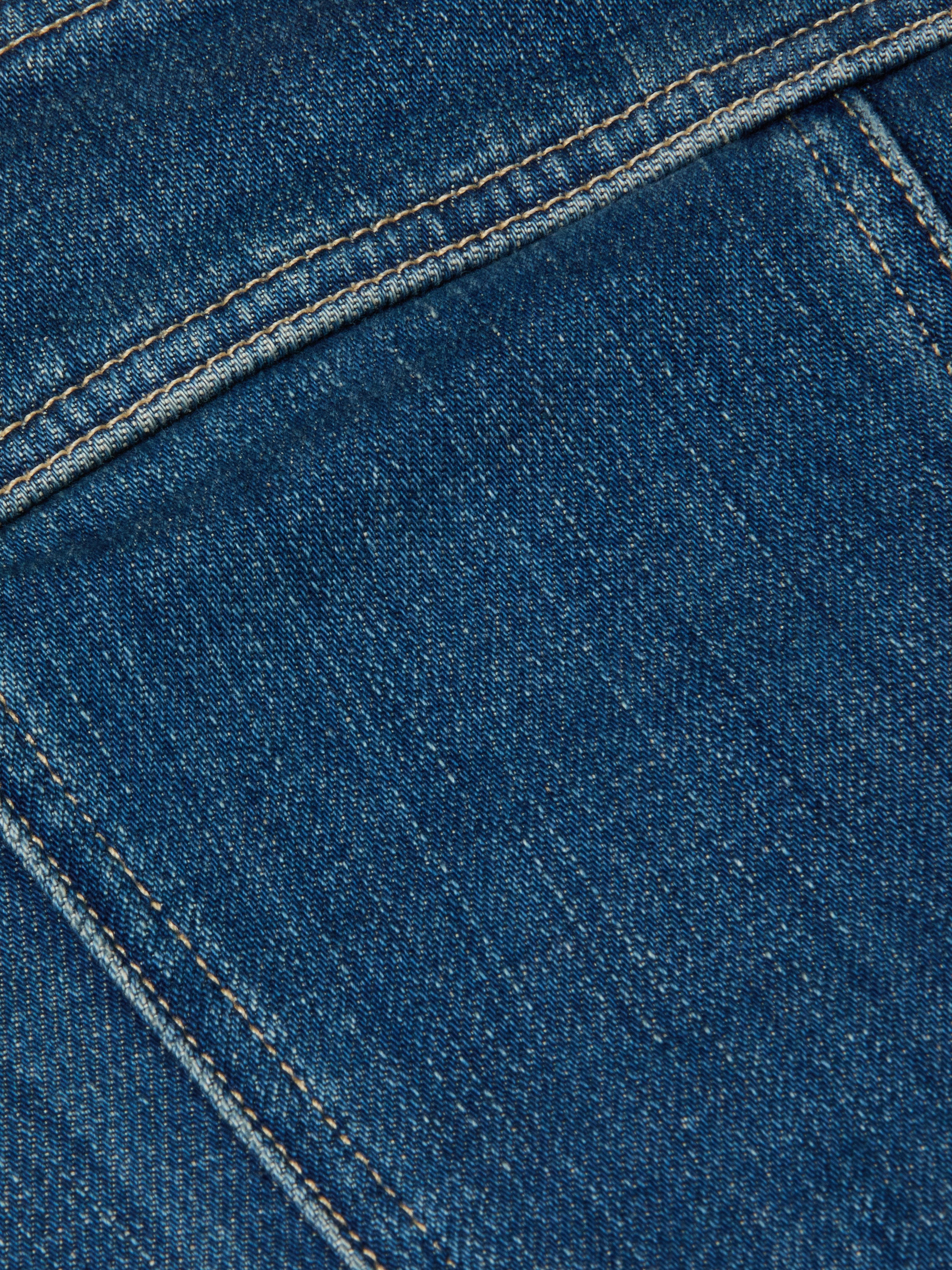 Close-up of the Lorda Dress in blue stretch denim fabric, highlighting detailed stitching, textured material, visible seams, and yellowish thread.