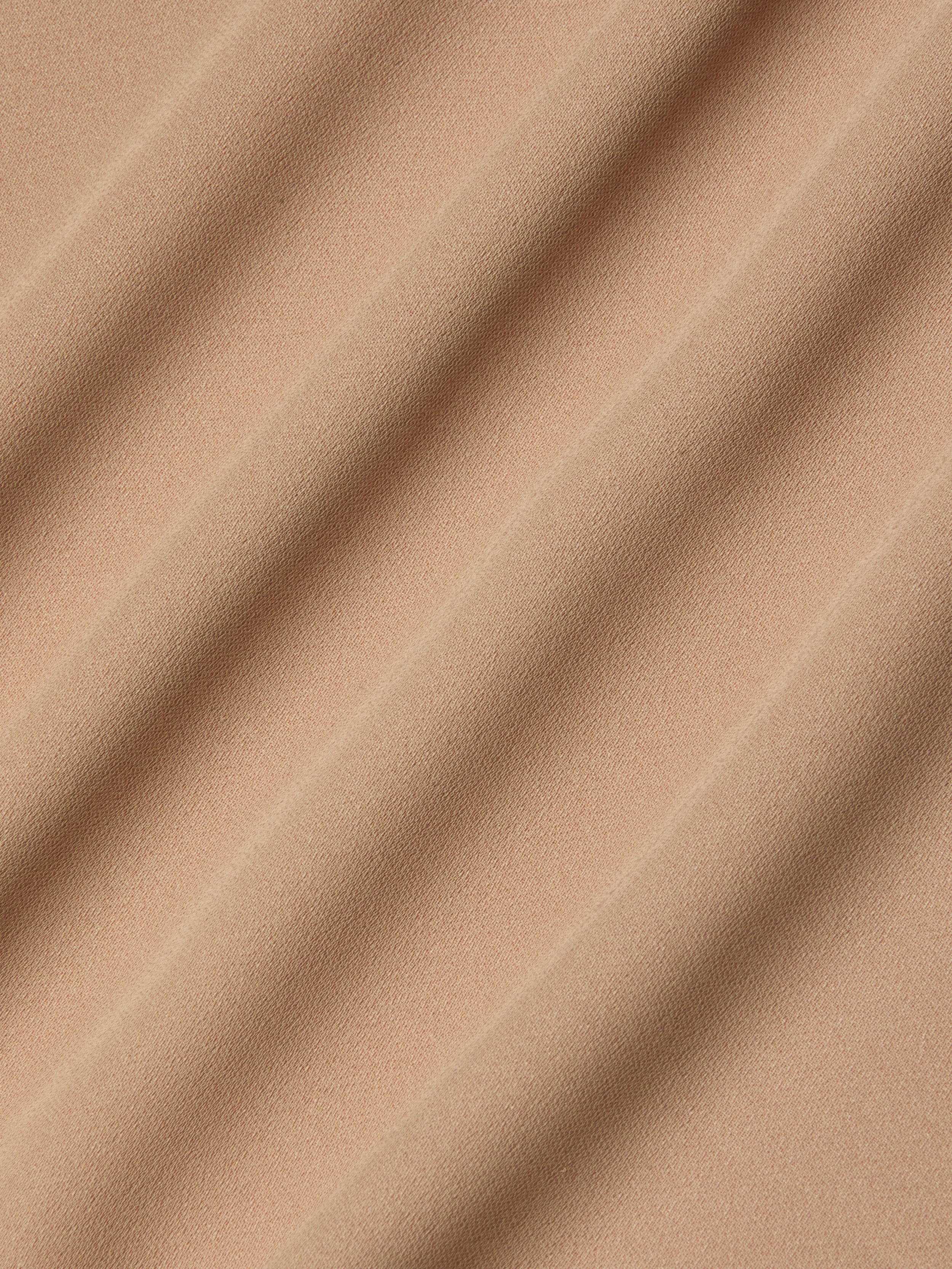 Close-up of beige poly georgette fabric with soft, diagonal waves and shadows, highlighting its smooth texture and gentle folds—an ideal choice for the Raye Slip Lining Dress featuring adjustable straps.