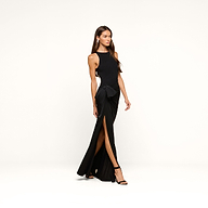 Wearing the Frost Gown—a sleeveless black tie dress featuring a high slit and a side bow—a woman walks confidently in black heels against a plain white background.