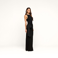 A woman stands in the Frost Gown, a sleeveless, floor-length black tie dress featuring a side sash detail, posing against a plain white background.