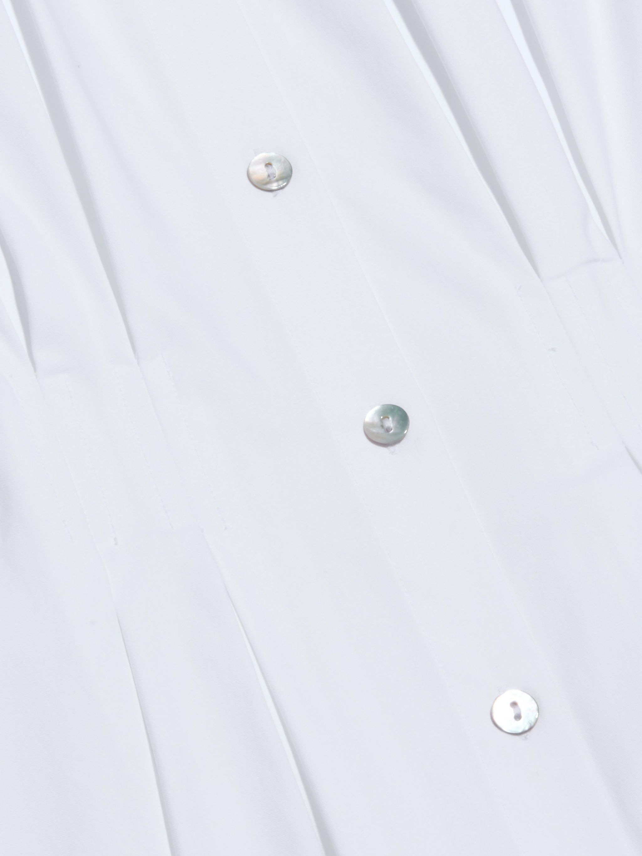 Close-up of the Journi Shirt Dress crafted from white cotton-blend poplin, featuring metallic buttons arranged in a vertical row. The smooth fabric is gently pleated near the buttons, creating a timeless silhouette.