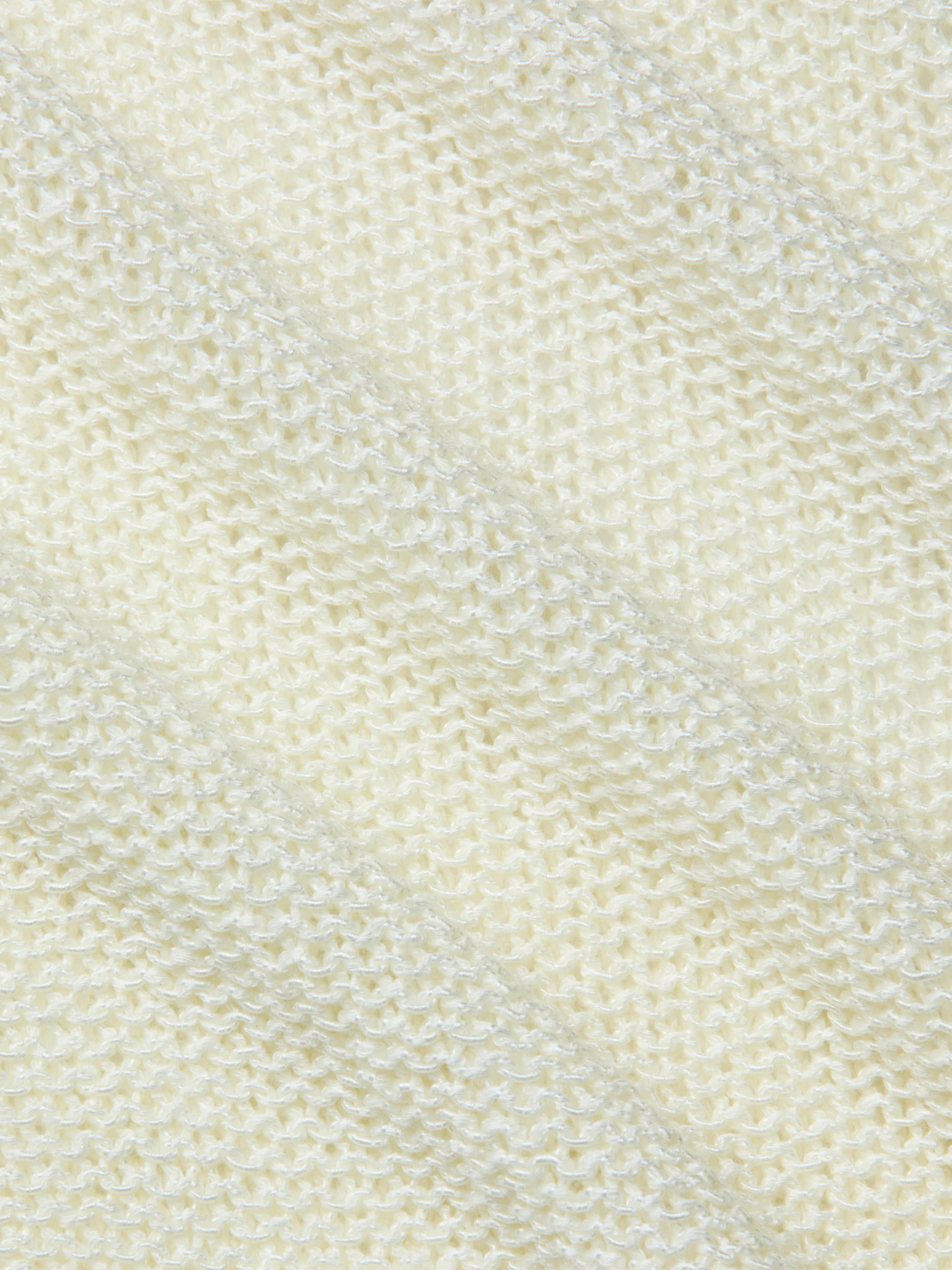 Close-up of the textured, cream-colored fabric of the Ethan Knit Pullover, featuring a diagonal ribbed pattern that highlights the fine stitches and softness of this knit garment.