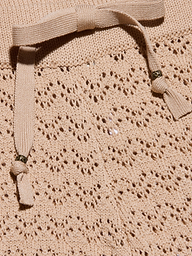 Primo piano del Gaelle Pointelle Knit Pant in beige, che mostra la sua intricata maglia a pizzo e la coulisse abbinata con accenti di perline metalliche: una scelta elegante e leggera per le vacanze.