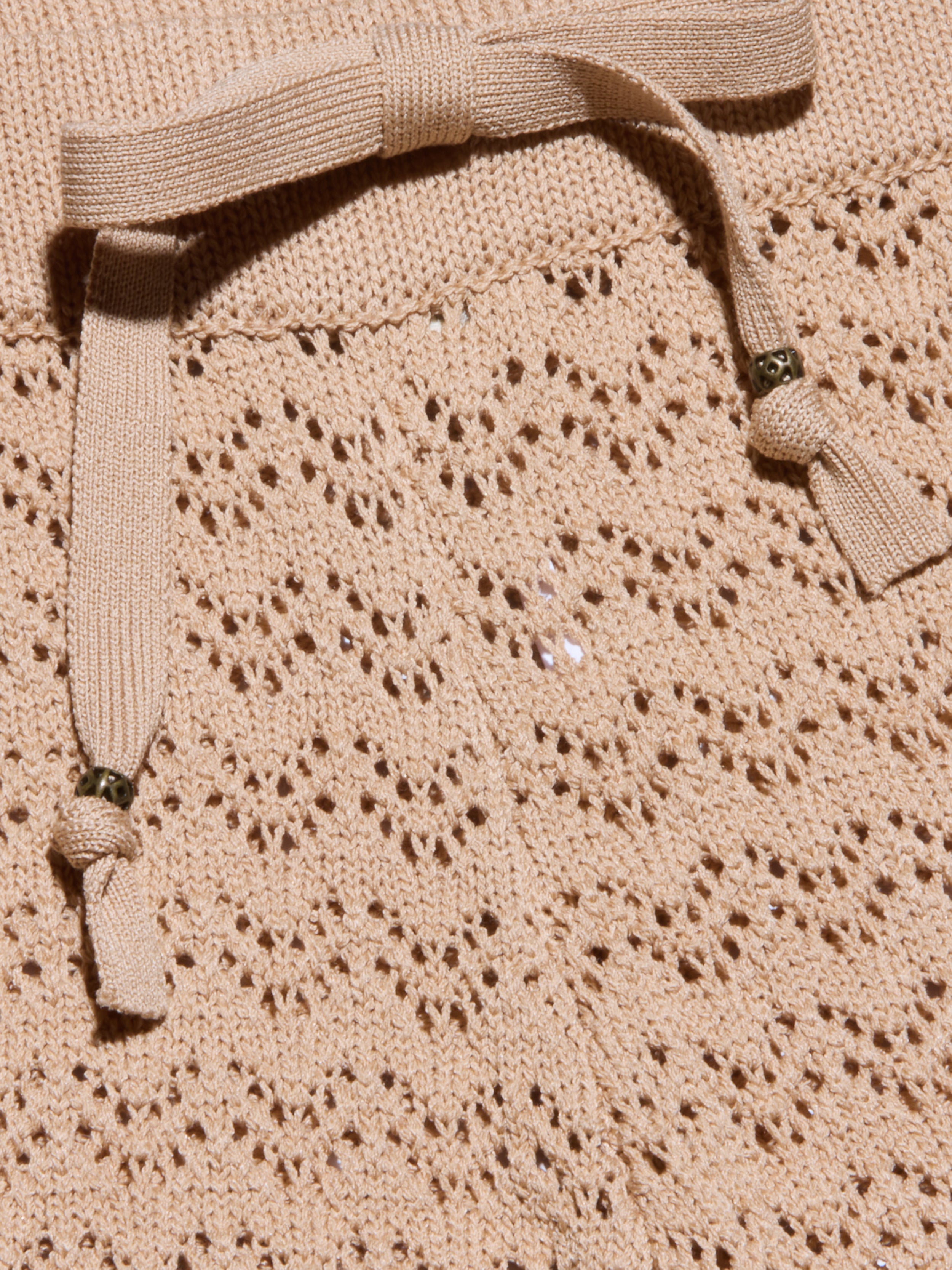 Primo piano del Gaelle Pointelle Knit Pant in beige, che mostra la sua intricata maglia a pizzo e la coulisse abbinata con accenti di perline metalliche: una scelta elegante e leggera per le vacanze.