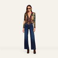 A woman wearing sunglasses, the Osiris Jacquard Cardigan with a tapestry print, a brown blouse, wide-leg blue jeans with a belt, and brown boots stands against a plain light background.