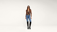 A woman stands against a plain white background, wearing a leopard print top, blue jeans, black knee-high boots, and sunglasses.