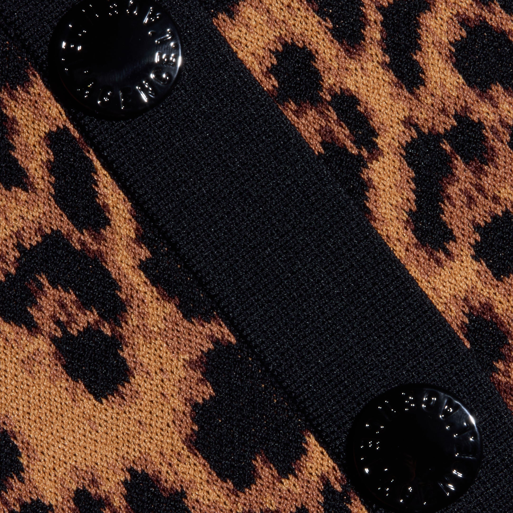 Close-up of the Osiris Jacquard Cardigan, featuring a brown and black leopard print in jacquard knit, a black textured vertical strip, and two round, shiny black buttons on the strip.