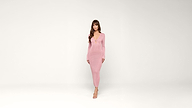 A woman in a long-sleeved, form-fitting pink dress and heels stands against a plain white background, facing forward with a neutral expression.