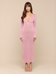 A woman stands facing forward against a plain white background, wearing the Sydney Knit Dress—a long-sleeve, pink maxi dress with a V-neckline and keyhole detail in pointelle knit—paired with open-toe heels.