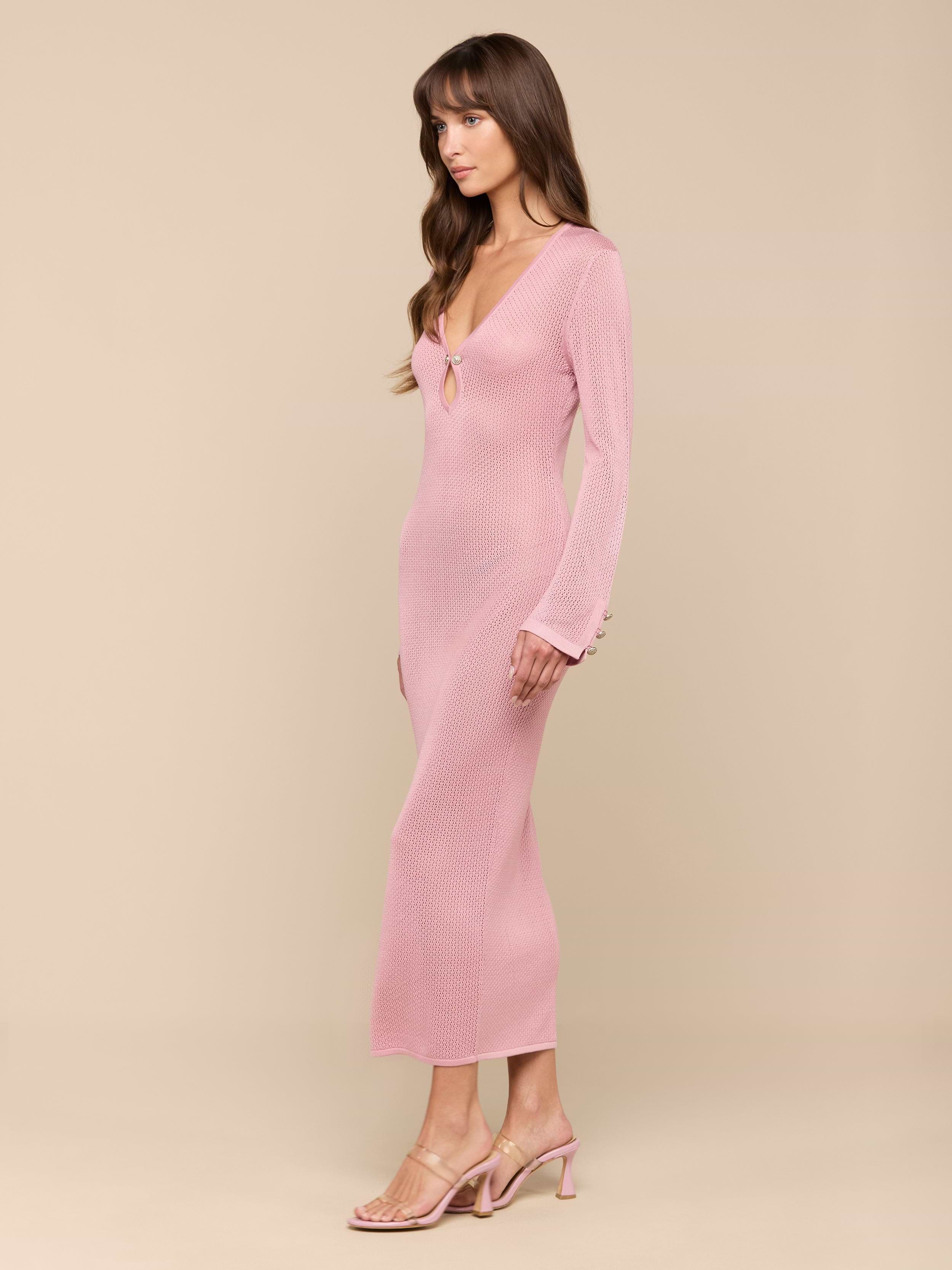 A woman in a fitted, long-sleeve pink Sydney Knit Dress and heeled sandals stands against a plain white background, posed in profile with her arms relaxed by her sides.