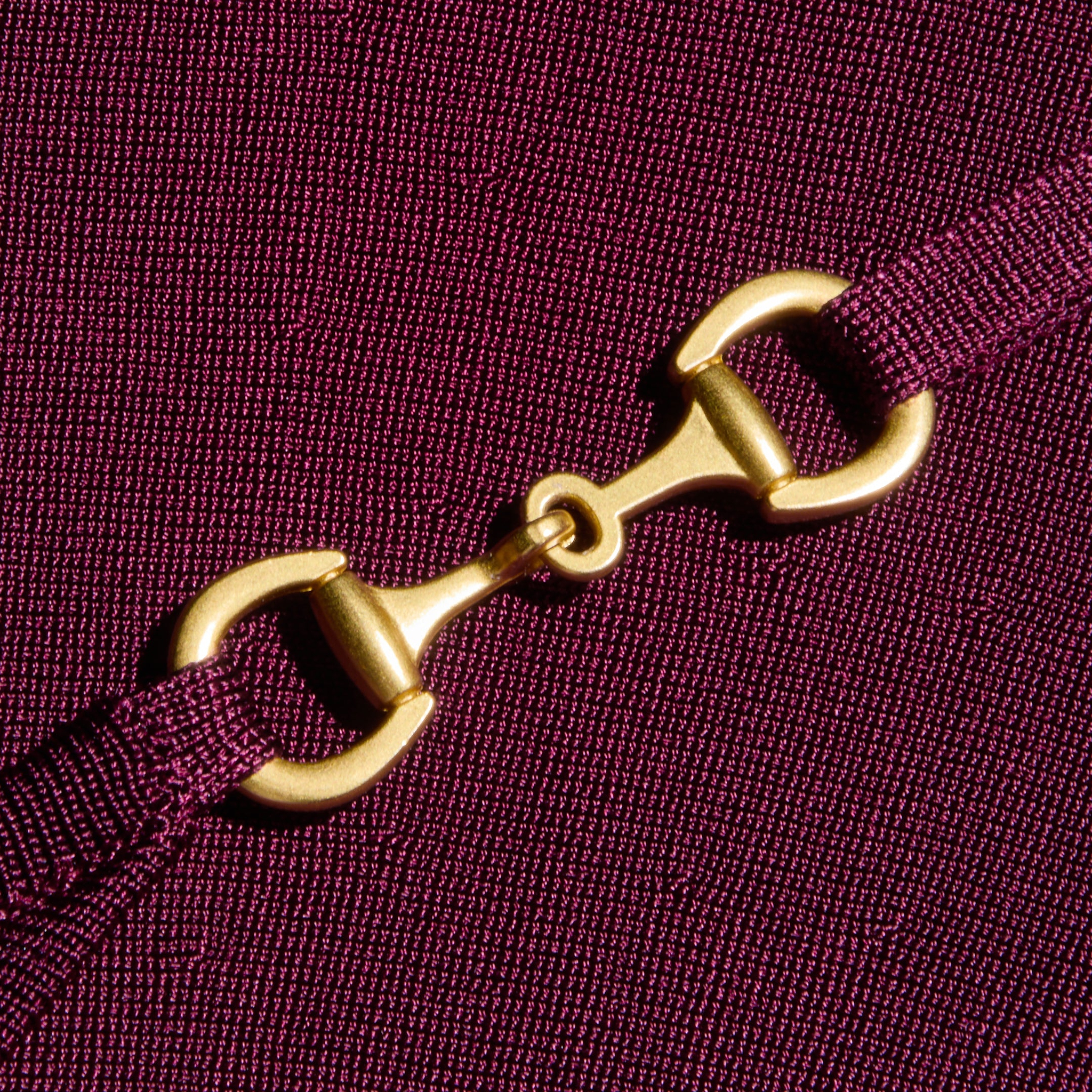 A close-up of a gold metal clasp connecting two ends of an adjustable purple strap, set against the textured stretch knit fabric of the Lana Flare Knit Dress.