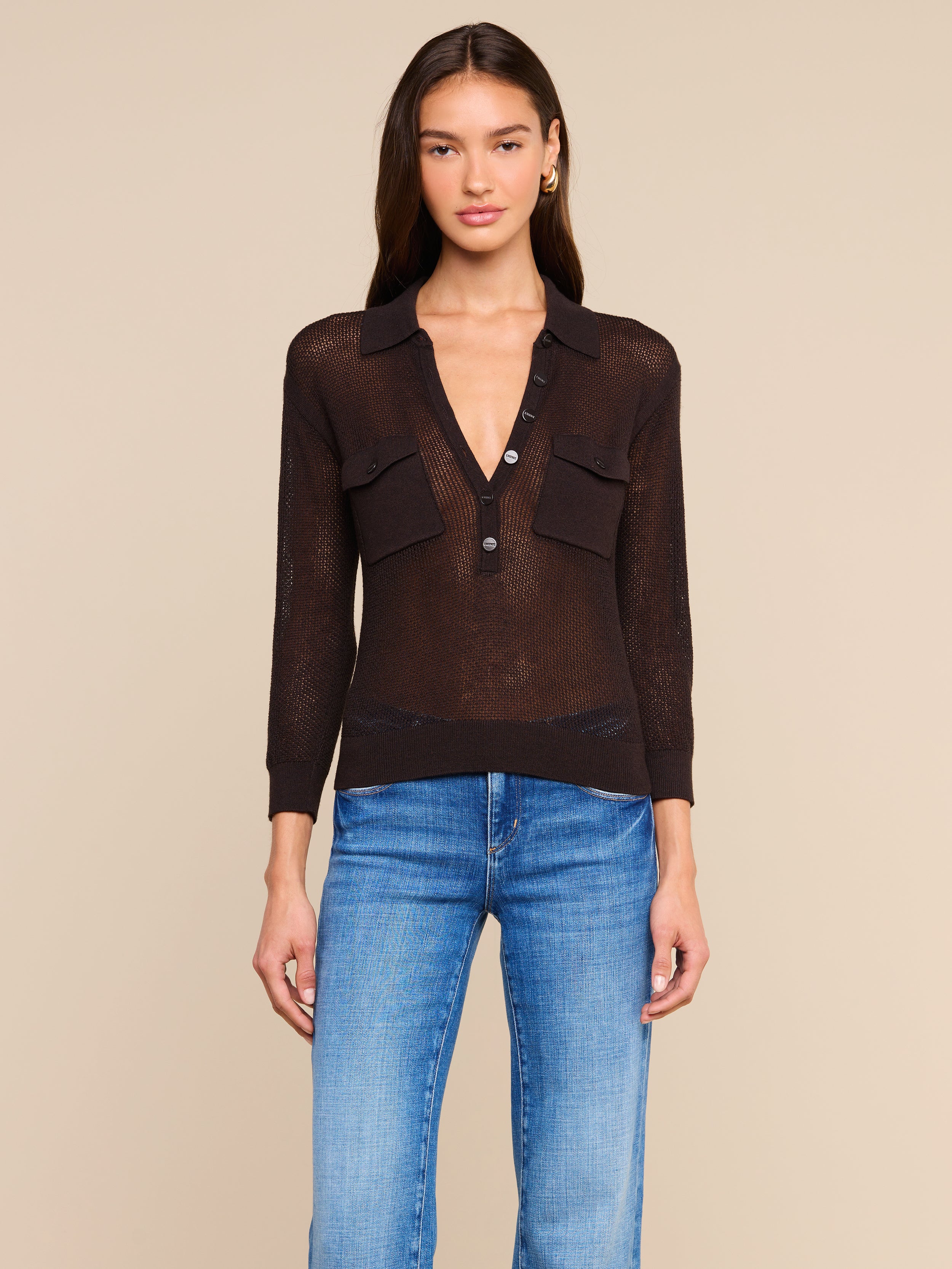 A woman stands facing forward wearing a sheer black long-sleeve Carine Top with two chest pockets and blue jeans, against a plain light background. The lightweight knit makes it perfect for Fall 2026.