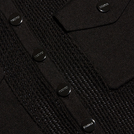 Close-up of a black lightweight knit Carine Top featuring shiny round buttons engraved with the word PRADA and a flap pocket. Perfect for Fall 2026.