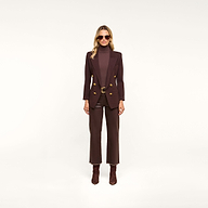 A woman stands facing forward against a plain light background, wearing sunglasses, brown pants, brown heeled boots, a brown turtleneck, and the Amelia Knit Blazer with gold buttons.