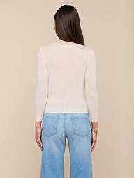A woman with long brown hair stands facing away, wearing the Eluna Cardigan Top and light blue jeans. Her arms rest by her sides against a plain, light background.