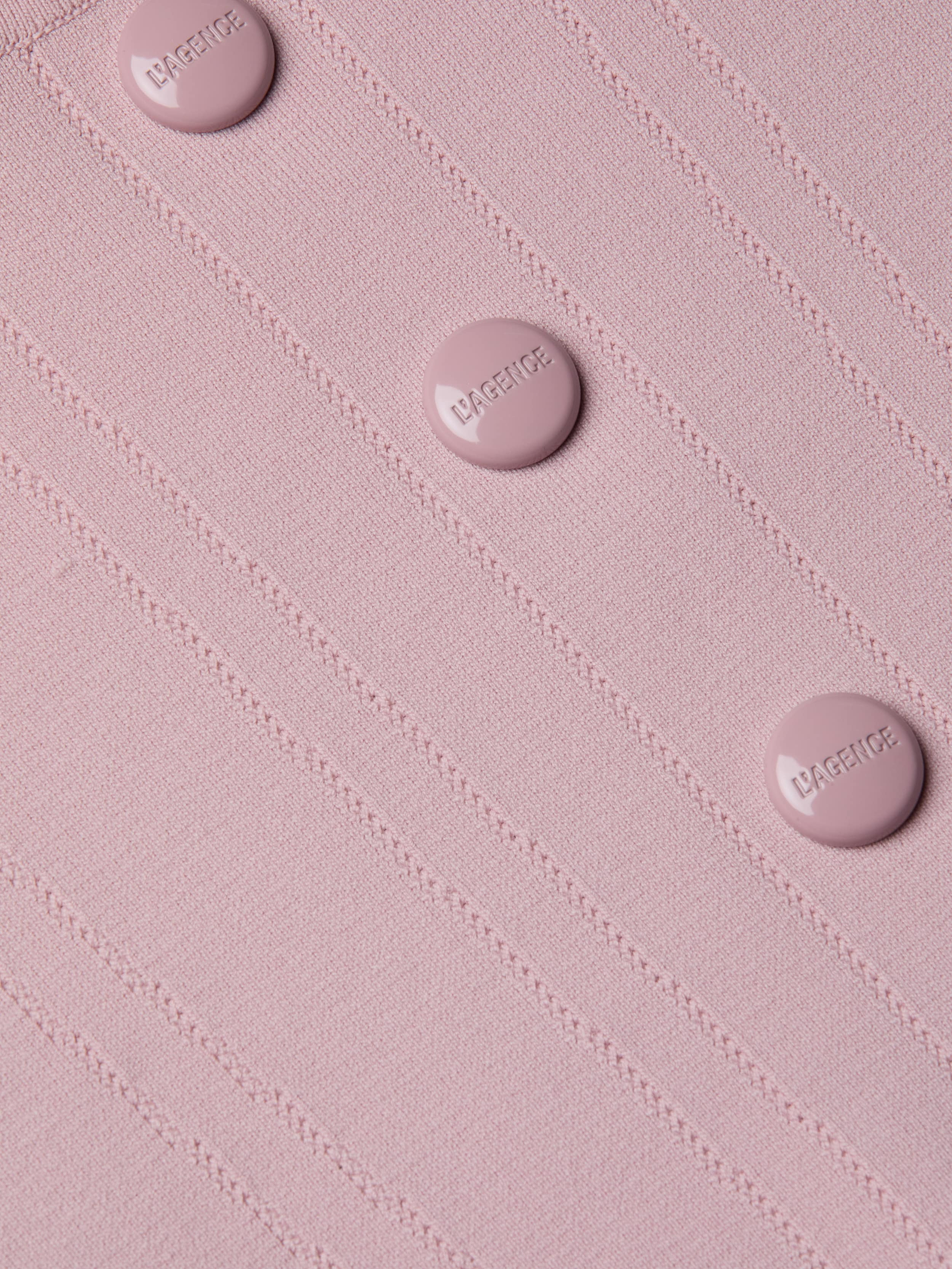 Close-up of the Dove Knit Corset Top, a light pink fitted piece featuring a ribbed power knit texture and four round buttons embossed with “LAGENCE” arranged in a neat vertical line. The design is finished with a subtle curved hemline.