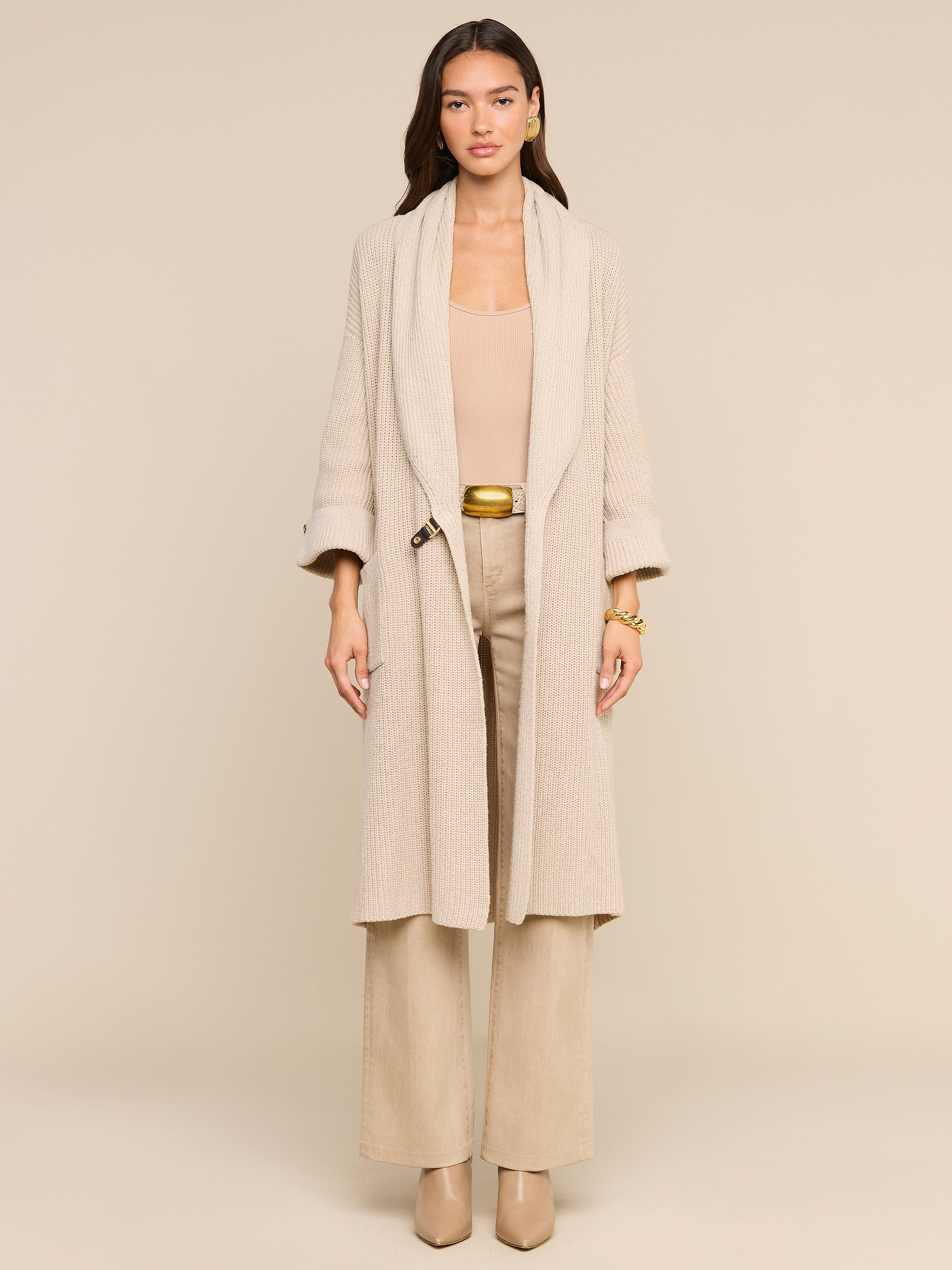 A woman stands facing forward against a plain white background, effortlessly exuding style in the Orielle Cardigan paired with wide-leg pants and heeled shoes, capturing the essence of timeless fall fashion.