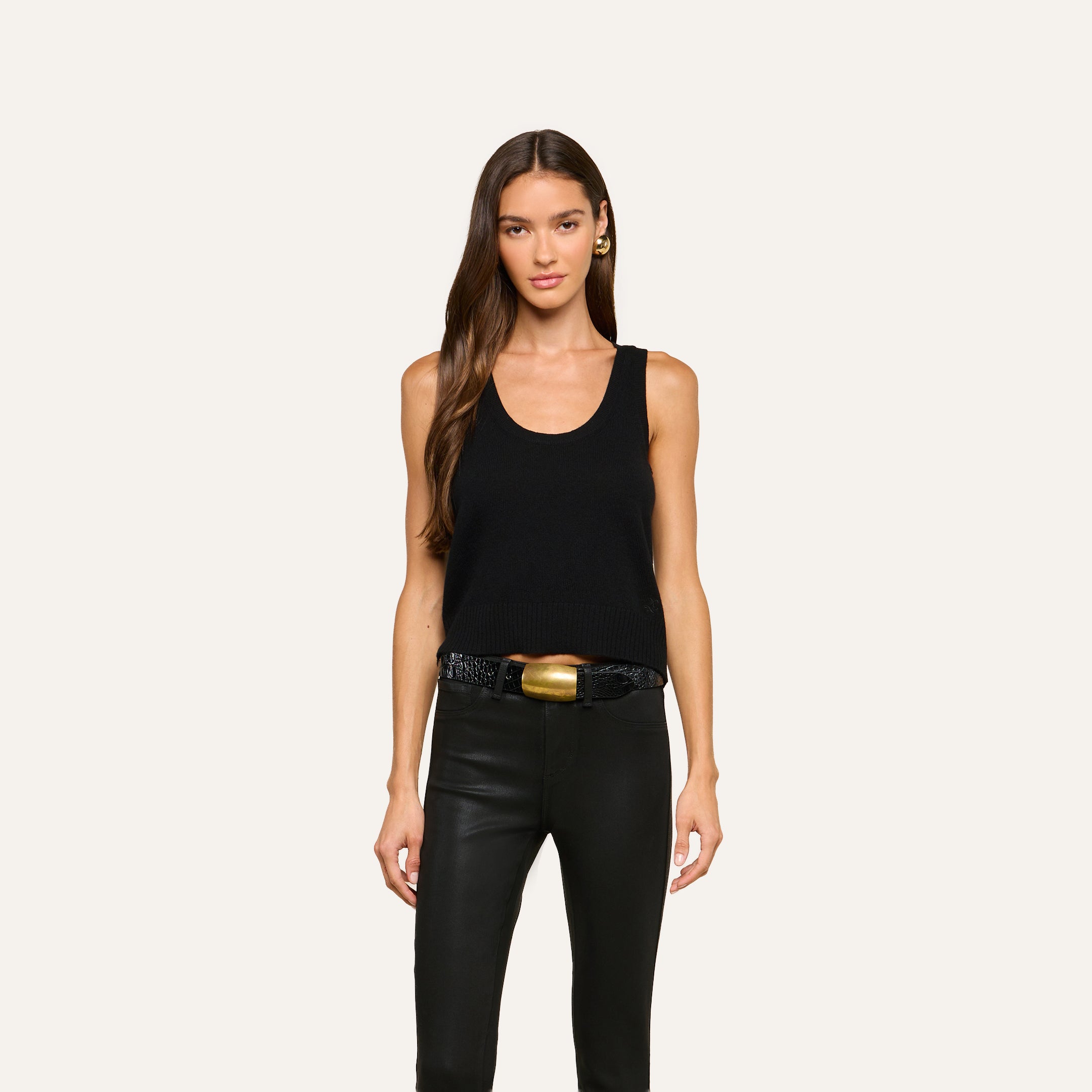 Woman with long brown hair wears the Filou Cashmere Tank, styled with black leather pants and a black belt featuring a large gold buckle, standing against a plain light background. Her look captures luxurious layering—ideal for an elevated, modern wardrobe.