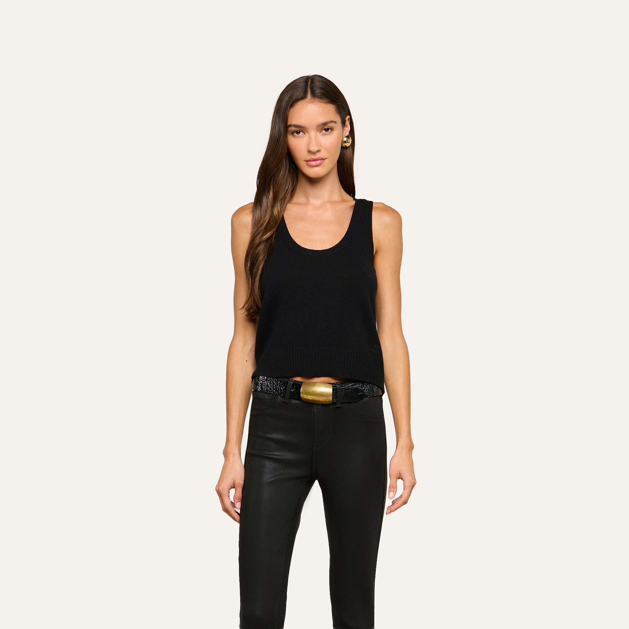 Woman with long brown hair wears the Filou Cashmere Tank, styled with black leather pants and a black belt featuring a large gold buckle, standing against a plain light background. Her look captures luxurious layering—ideal for an elevated, modern wardrobe.
