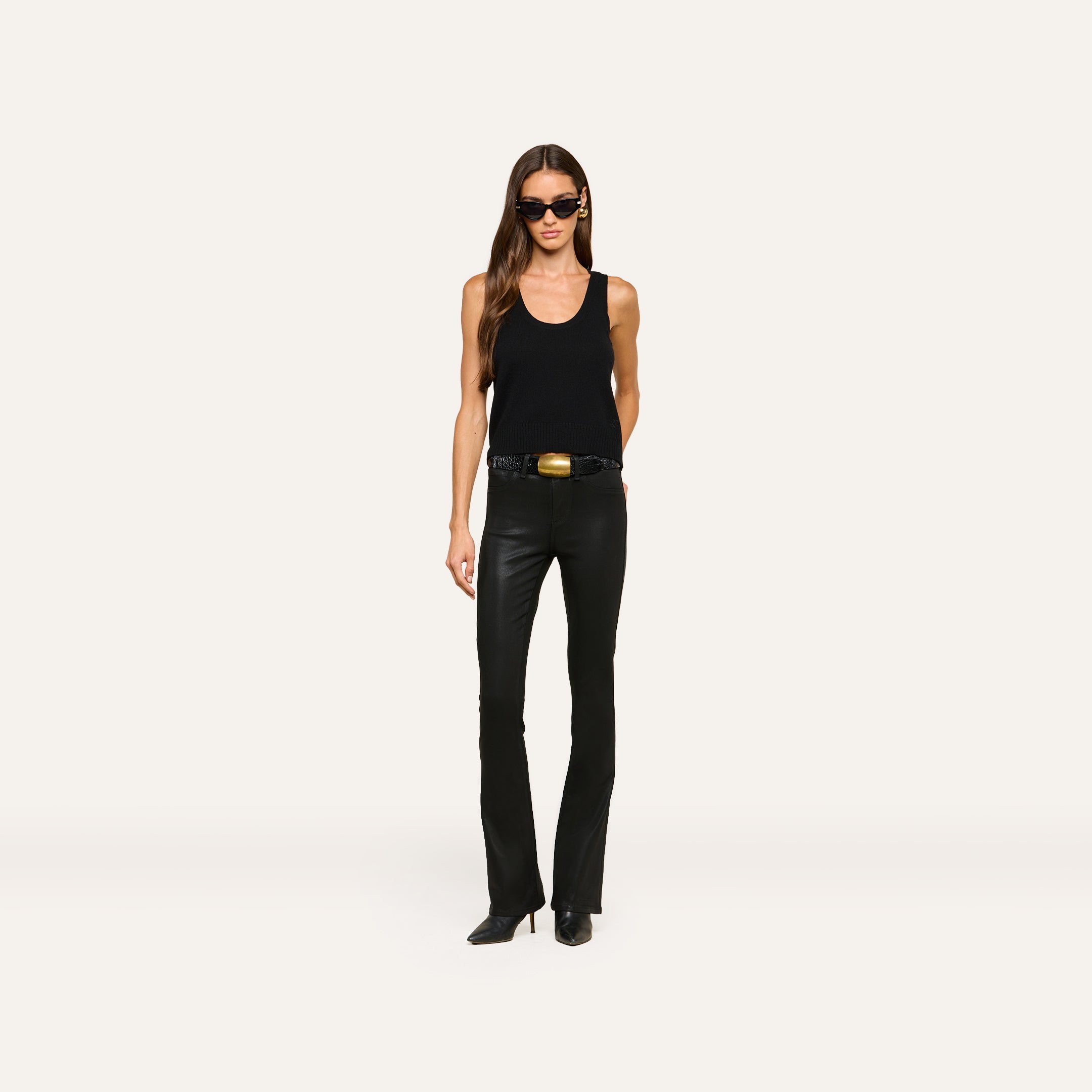 A woman wearing the Filou Cashmere Tank in black, paired with black leather pants, a black belt with a gold buckle, black pointed boots, and sunglasses stands against a plain white background.