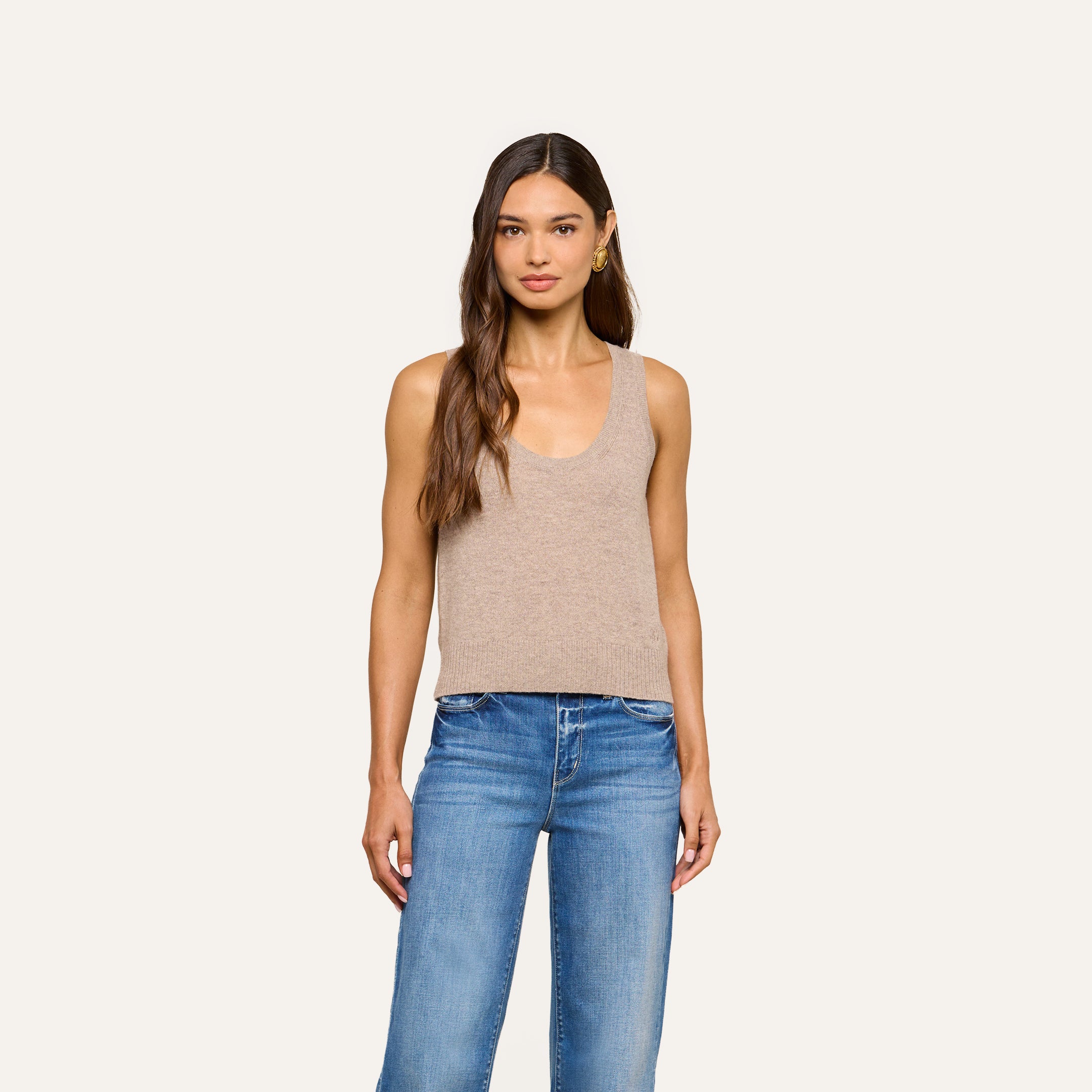 A woman with long brown hair wears the Filou Cashmere Tank in beige paired with blue jeans, standing against a plain light background, facing forward with a neutral expression.
