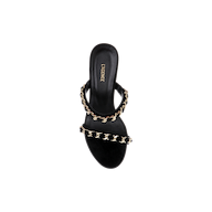 The Sarika Chain Sandal is a black suede, open-toe high-fashion sandal highlighted by two gold chain-embellished straps and “L’AGENCE” inscribed on the insole, shown against a white background.