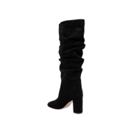 The Fletcher Boot, a black knee-high slouchy suede boot featuring a rounded toe and high block heel, is displayed against a plain white background for a touch of bohemian chic style.